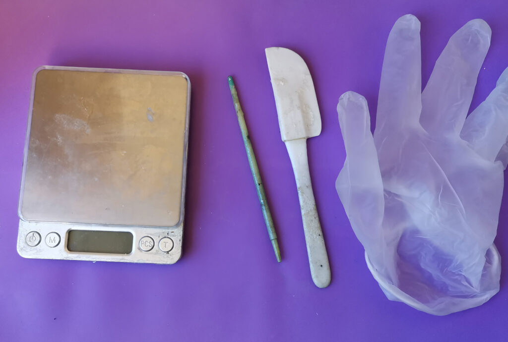 photo of a weighing scale, the end of a paintbrush, a small baking spatula and a vinyl glove